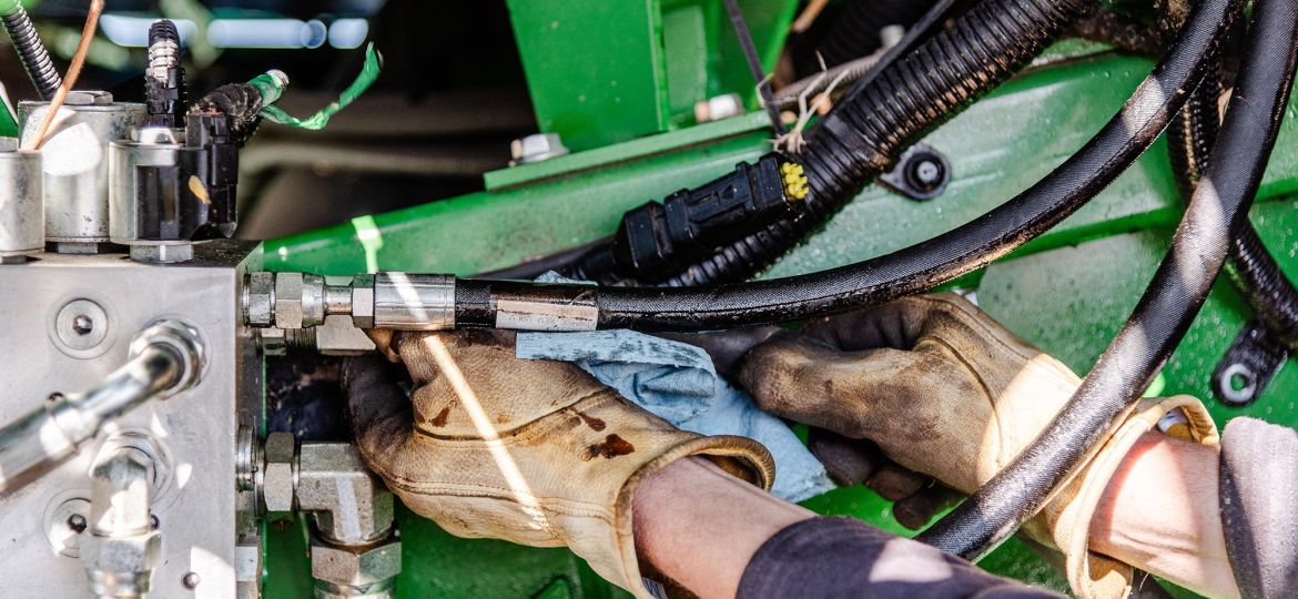 Farmer,Repairing,Hydraulic,Hose,Under,Combine,Undercarriage,,Wearing,Yellow,Gloves,
