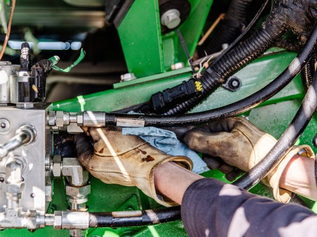 Farmer,Repairing,Hydraulic,Hose,Under,Combine,Undercarriage,,Wearing,Yellow,Gloves,
