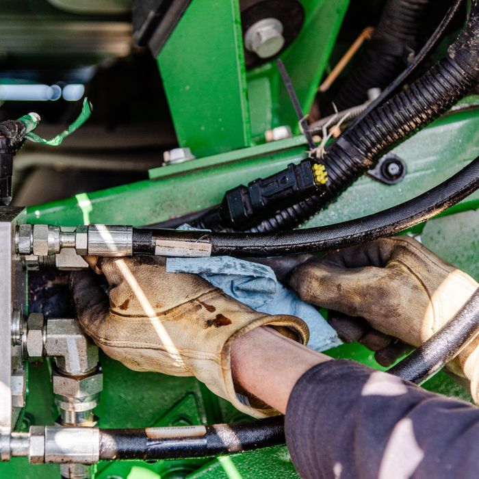 Farmer,Repairing,Hydraulic,Hose,Under,Combine,Undercarriage,,Wearing,Yellow,Gloves,